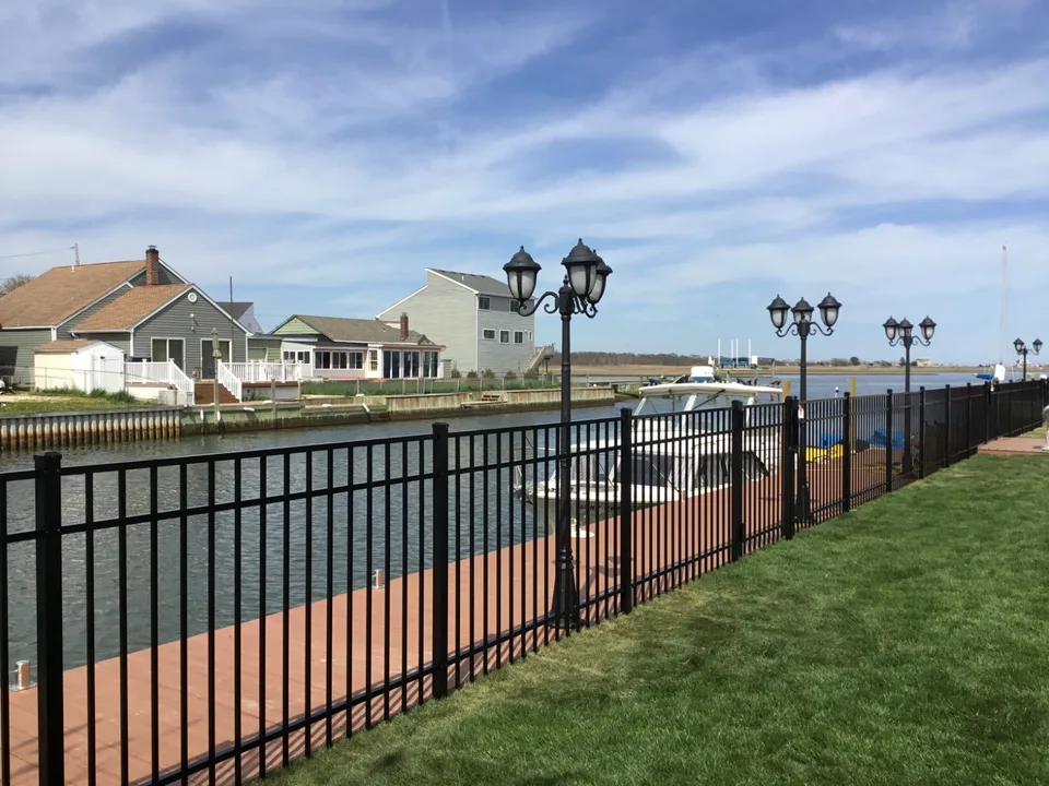 Four-foot black aluminum fence defining a canal-side residential yard in Mastic Beach, New York.