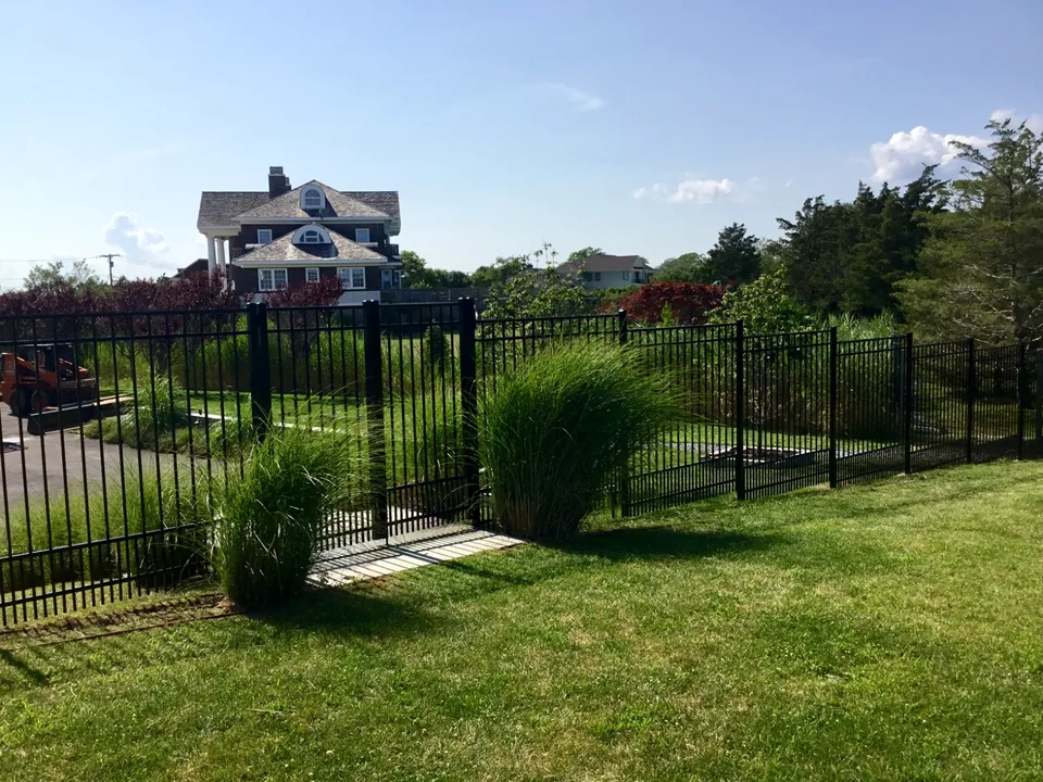Six-foot black aluminum fence integrated with residential landscaping in Westhampton, New York.