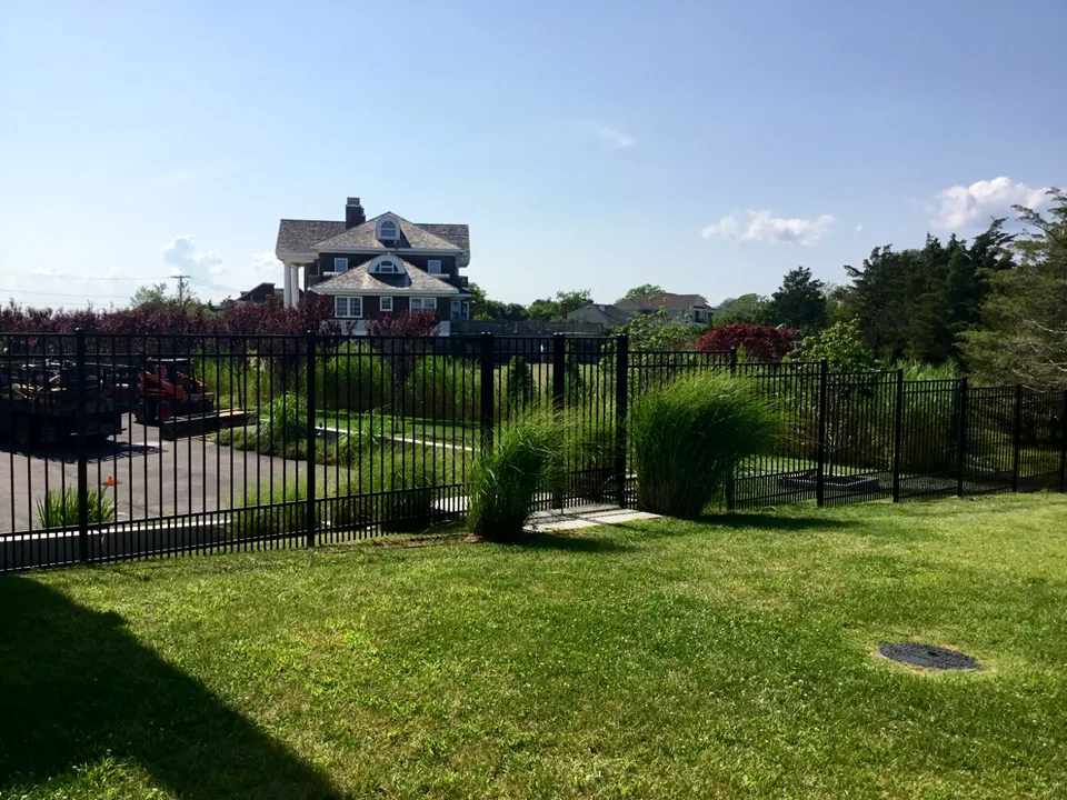 Six-foot black aluminum fence stepping with a landscaped grade in Westhampton, New York.