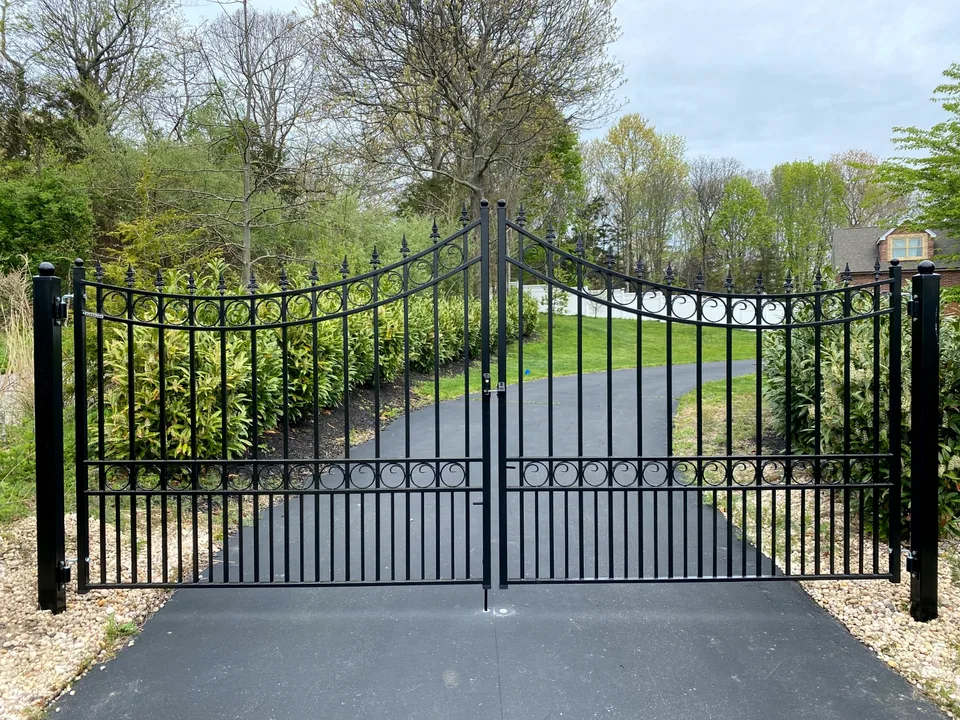 Decorative black steel driveway gate with scrollwork and spear details in Calverton, New York.