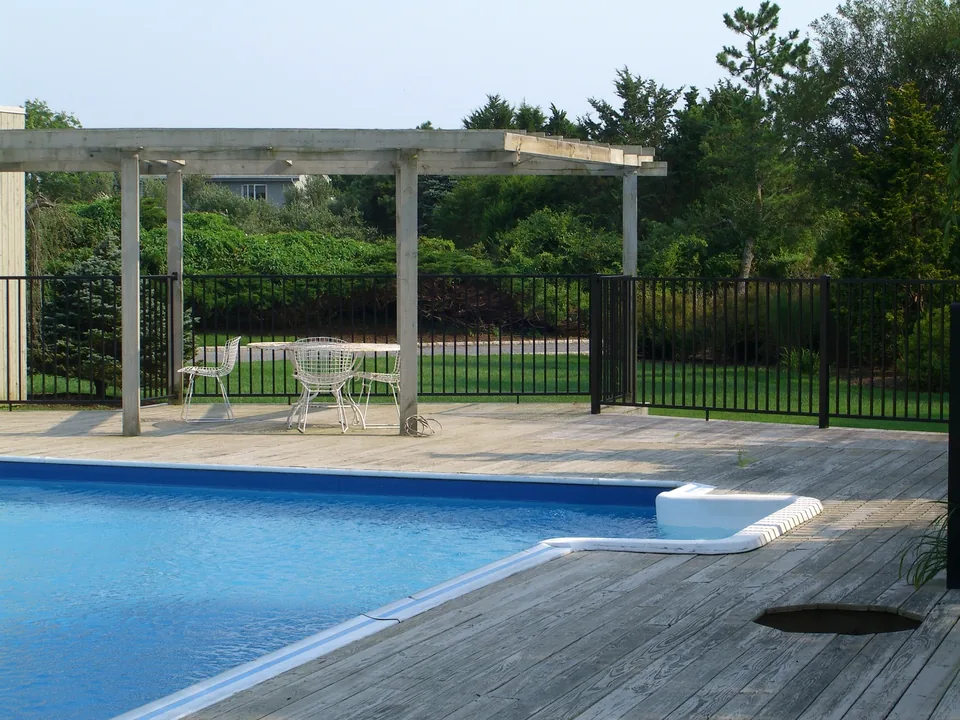 Four-foot black aluminum pool fence installed around a pool on a wood deck in Southampton, New York.