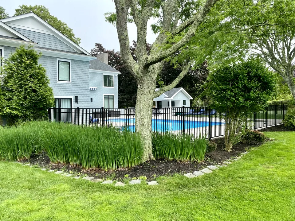 Black Style 202 aluminum pool fence integrated with mature landscaping in Remsenburg, New York.