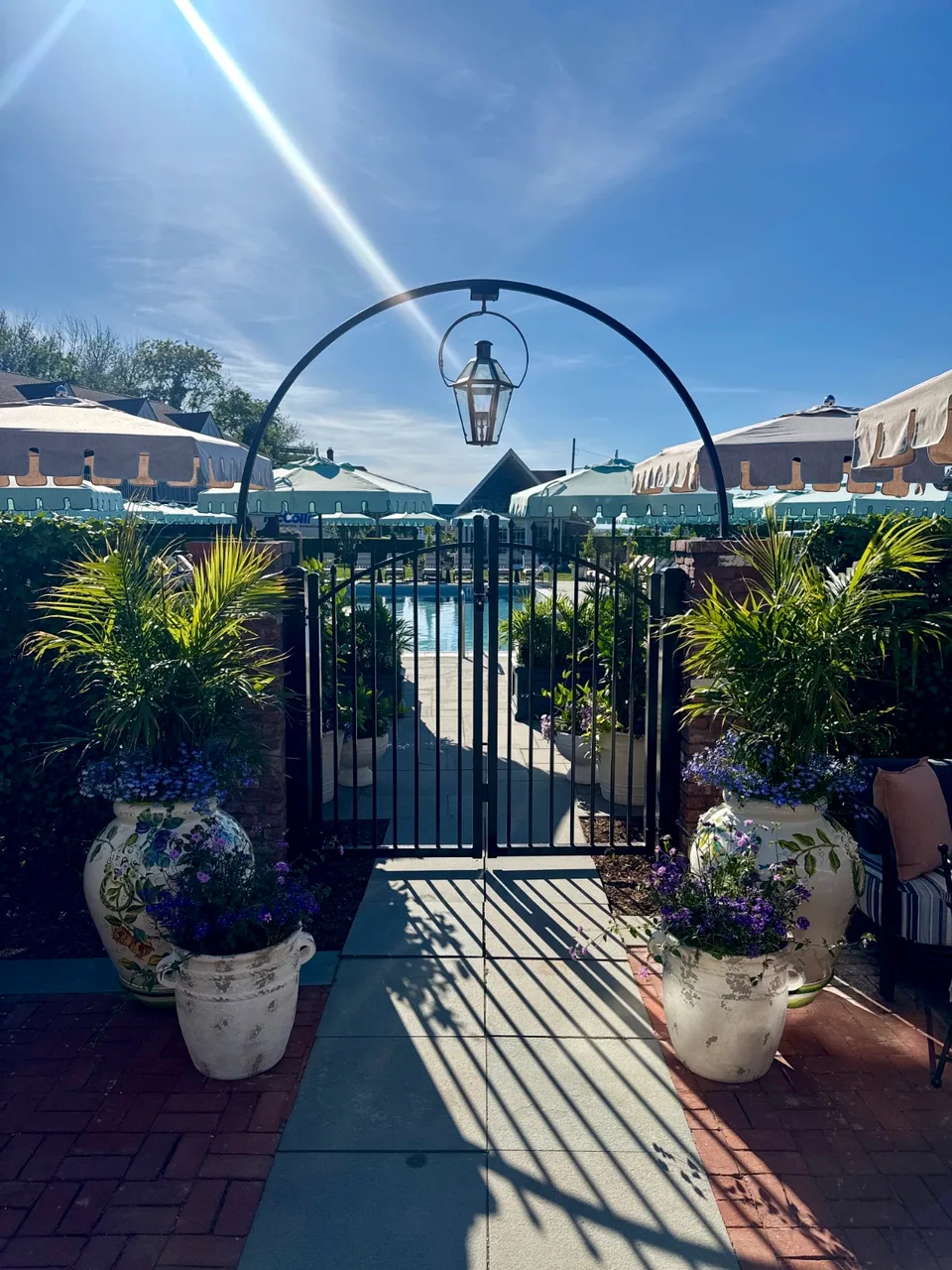 Six-foot black aluminum entrance gate leading to a resort pool patio in Sag Harbor, New York, with a gas lantern overhead.