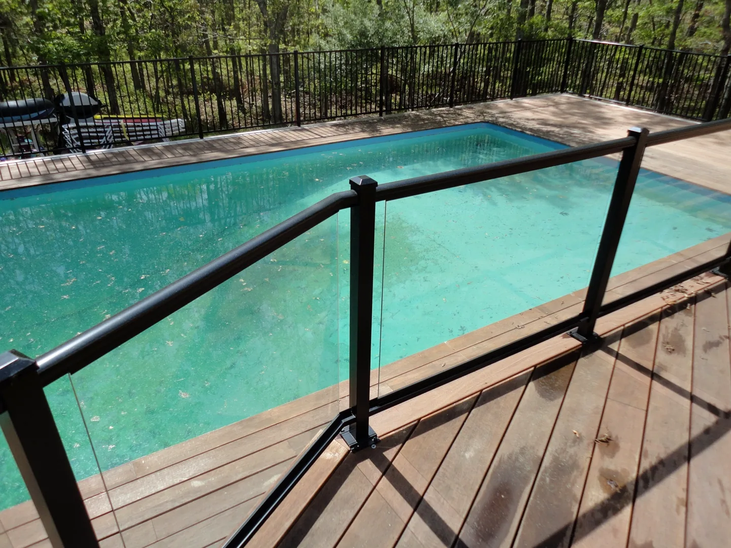 Close view of the aluminum-framed glass railing following the angled edge of the wood deck above the pool in Southampton, New York