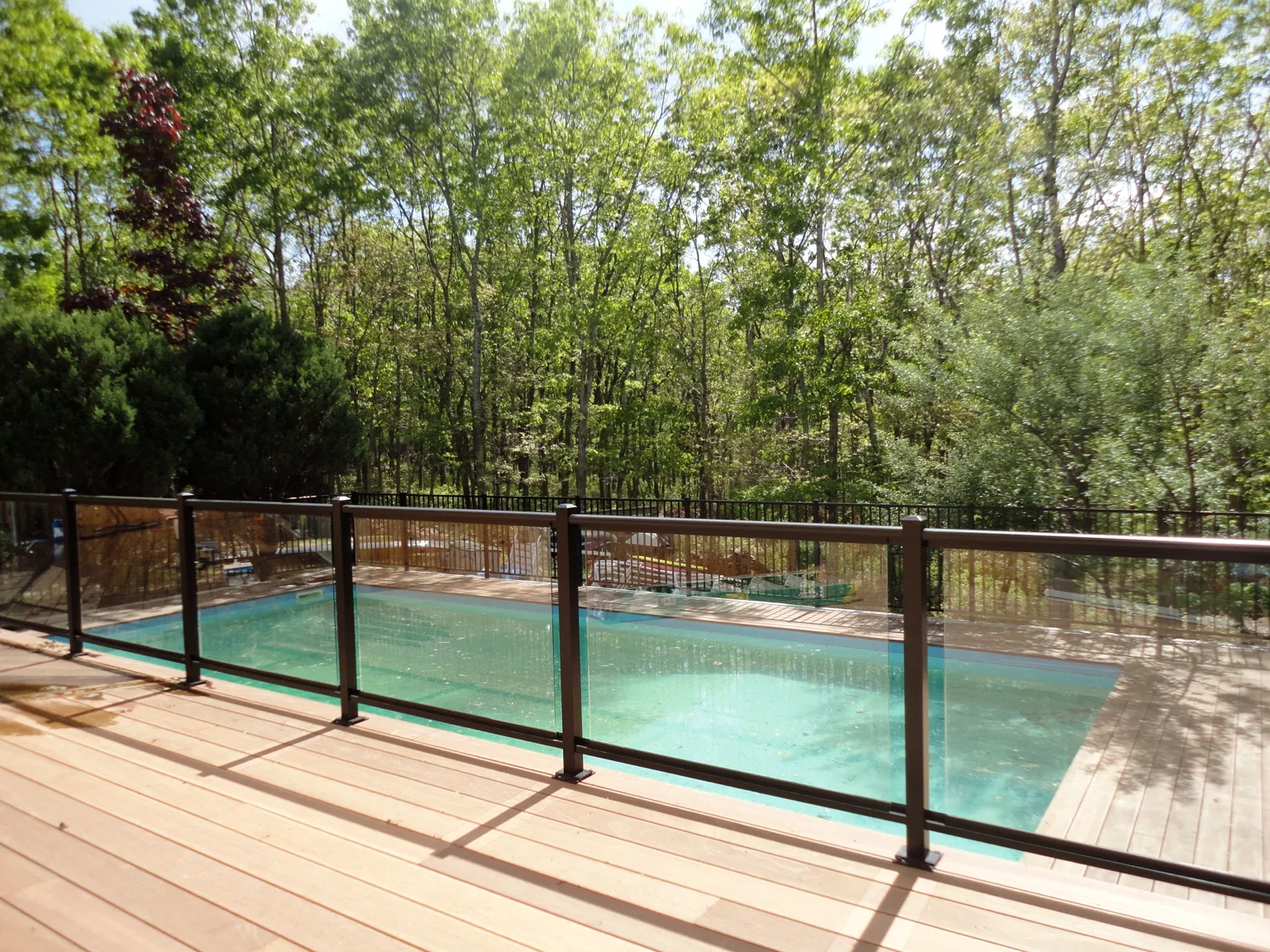 View through the aluminum-framed glass railing toward the swimming pool and wooded yard in Southampton, New York