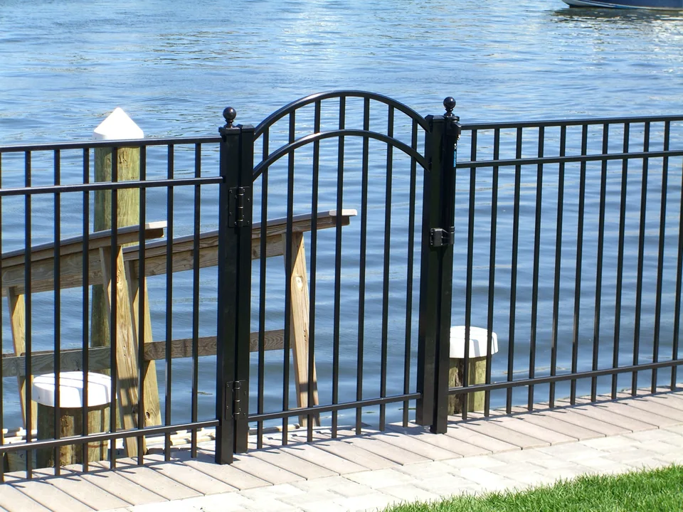 Arched black aluminum gate in a waterfront fence beside a dock in Seaford, New York
