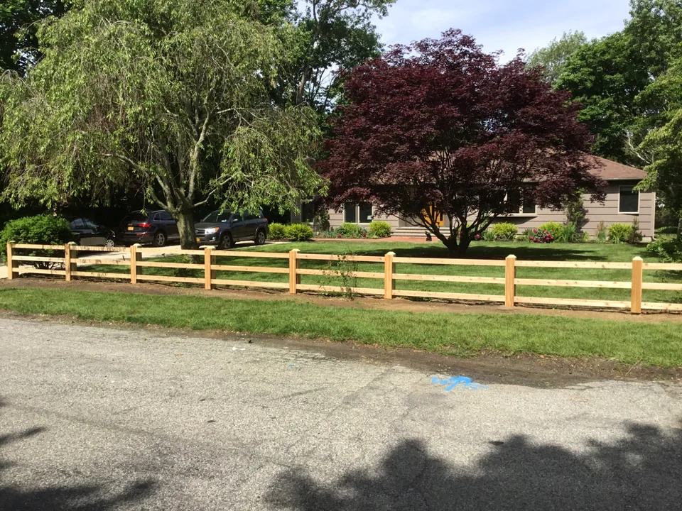 Wide view of custom three-rail board fencing at a Bellport home.