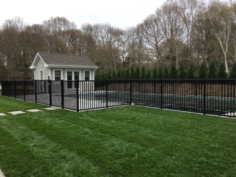 Four-foot black aluminum pool fence with a gate enclosing an inground pool beside a shingled pool house in East Hampton, New York