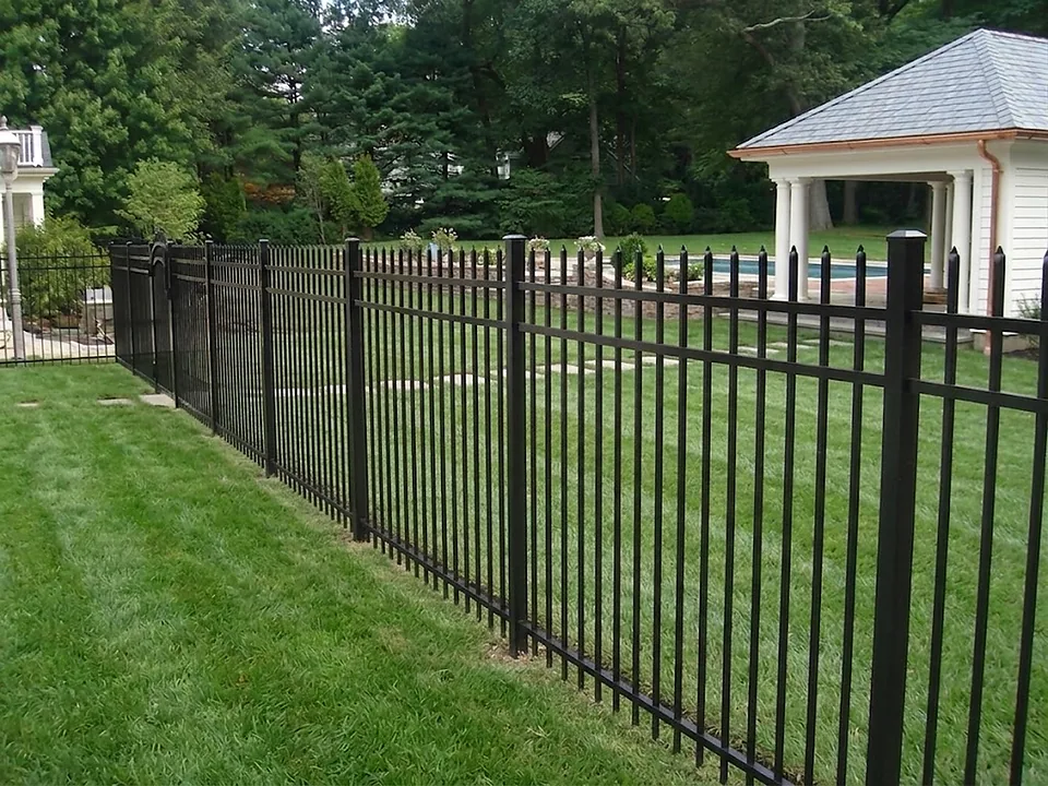Five-foot black Jerith aluminum pool fence with spear-top pickets and an arched gate section, enclosing a pool beside a slate-roofed poolhouse with white columns in Syosset, New York
