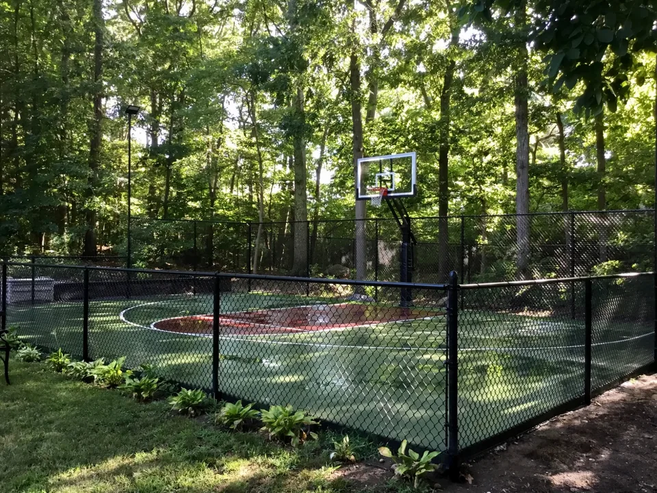 Black chain link basketball court enclosure integrated with mature woodland landscaping