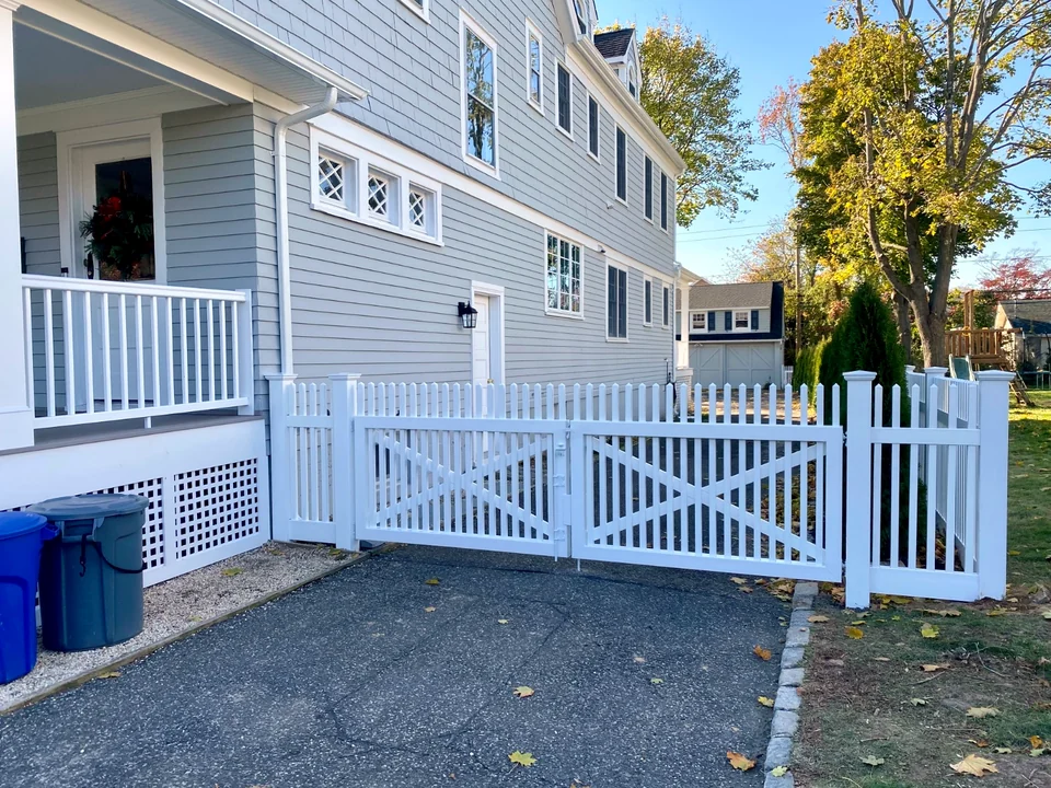 White PVC crossbuck-style double driveway gate with matching picket fencing in Brightwaters, New York.
