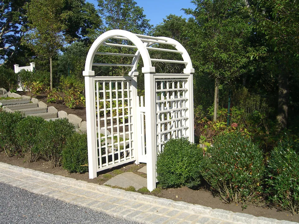 Four-foot-wide freestanding cedar arbor stained white with an arched top and square lattice sides, framing bluestone garden steps in Montauk, New York