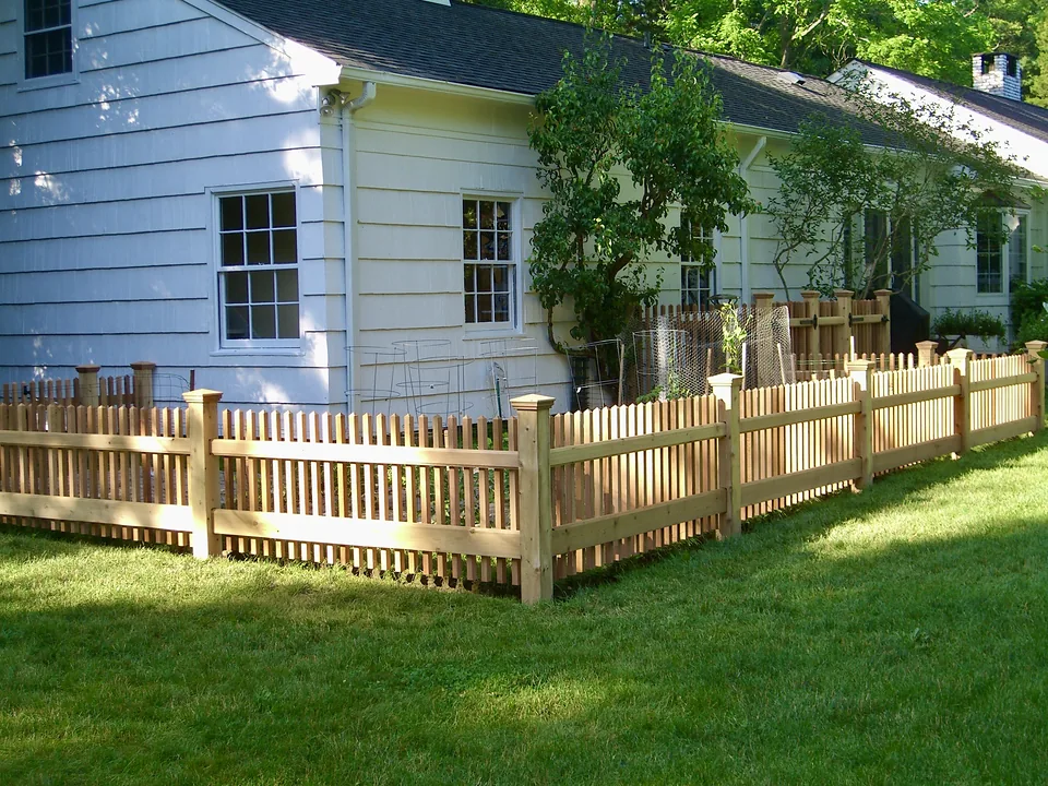 Three-foot cedar picket garden fence with capped posts enclosing a kitchen garden beside a white shingled house in Lloyd Neck, New York
