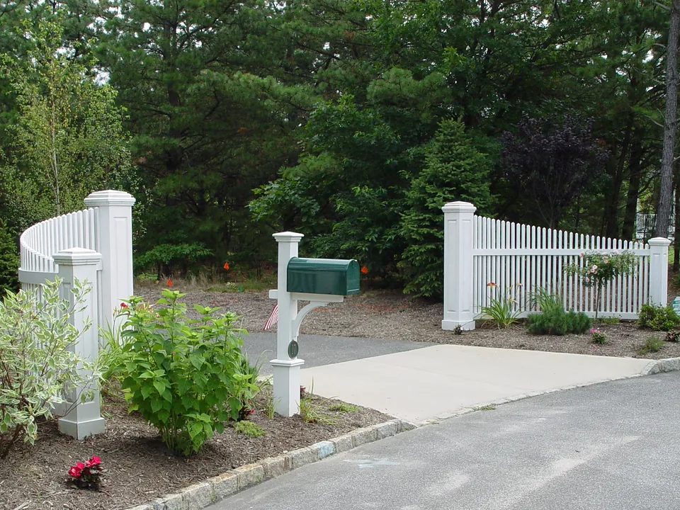 A pair of curved cedar picket panels stained white flanking a driveway entrance either side of a mailbox in Manorville, New York