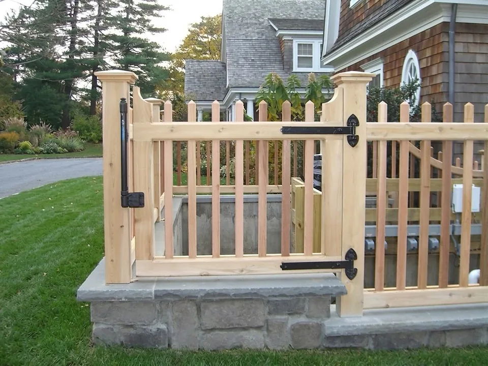 Detail of a cedar pool equipment enclosure gate showing black strap hinges, a self-closing hinge and scalloped rails, in Oyster Bay, New York