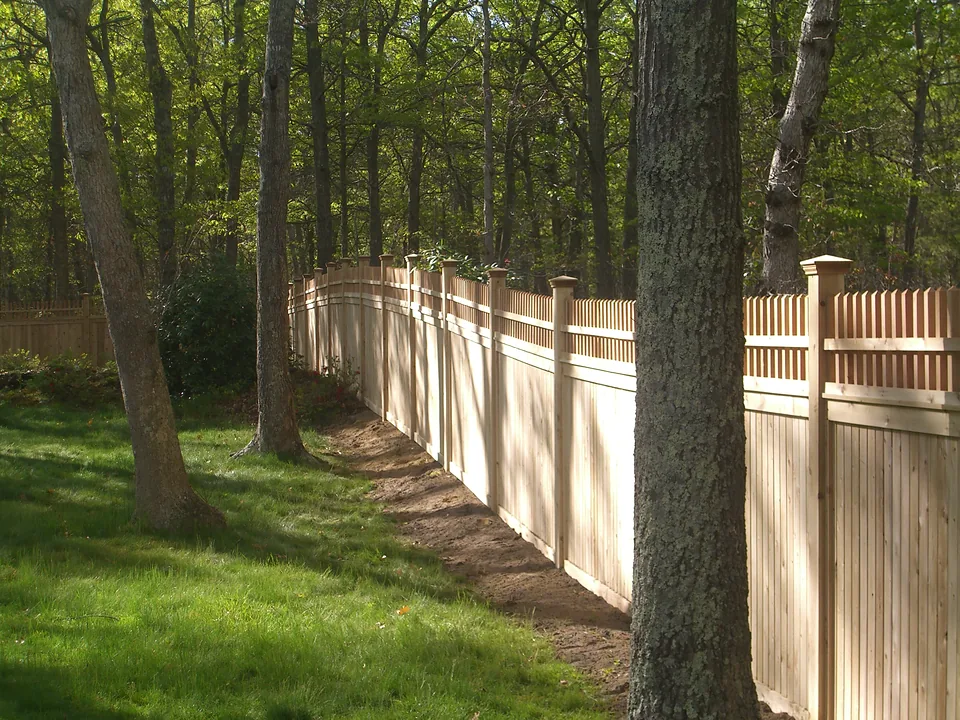 Six-foot cedar tongue and groove privacy fence with an eighteen-inch Victorian topper on capped 5x5 cedar posts, curving away through oak woods in Bridgehampton, New York