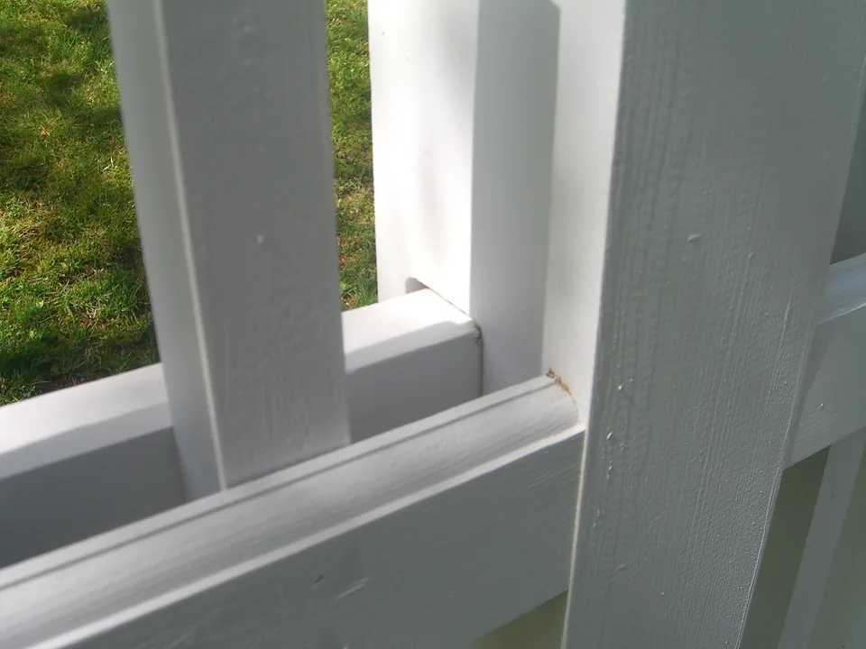 Close detail of a white cedar Victorian picket fence showing the rail passing through the post and the chamfered picket tops, in Larchmont, New York