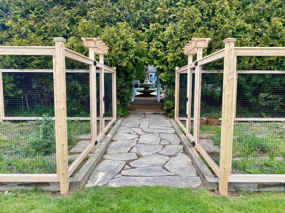 Stone path leading to paired cedar arbor gates at a wire garden enclosure in Sagaponack, New York