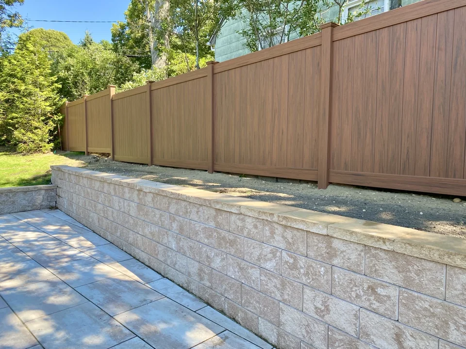 Angled genuine view of the cedargrain PVC privacy fence running above the Sag Harbor retaining wall