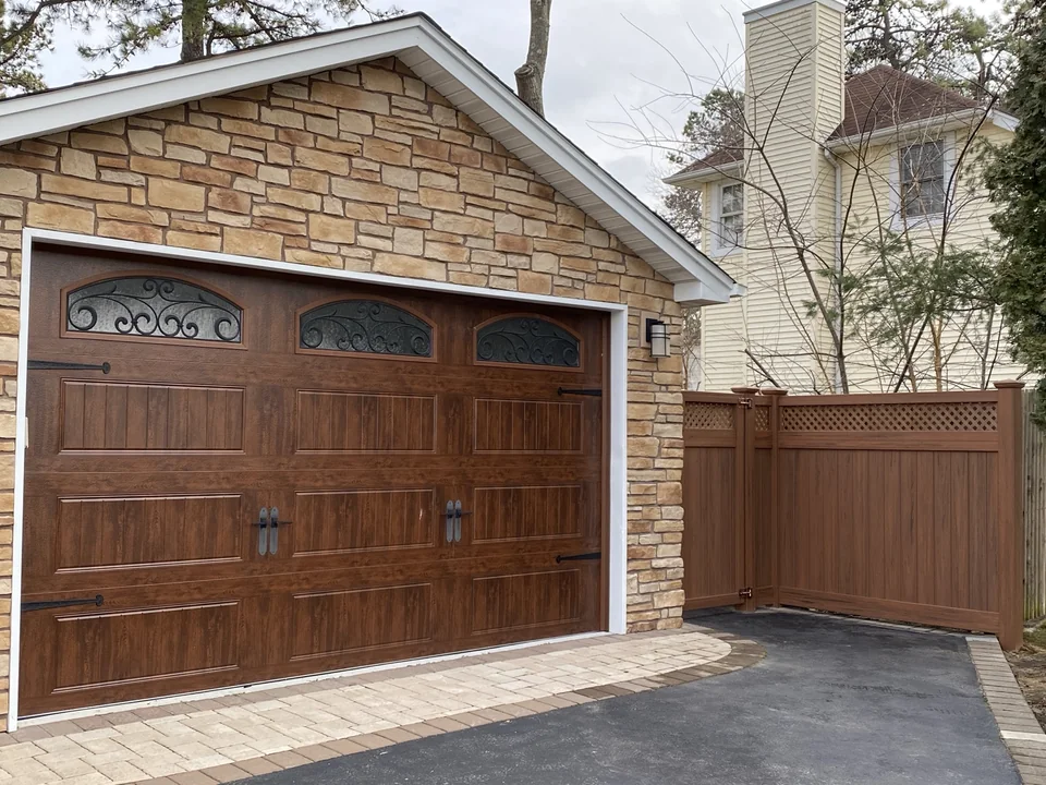 Cedargrain PVC privacy fence beside a wood-tone garage door and stone exterior in West Islip, New York