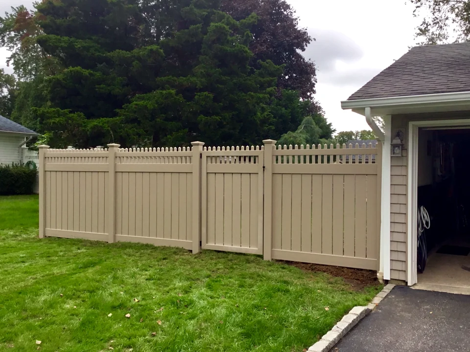 Tan PVC privacy fence with a decorative picket top and matching walk gate beside a Coram home.