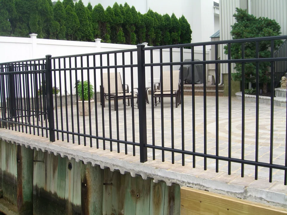 Water-side view of black aluminum fence installed along a raised masonry patio and bulkhead in Seaford, New York