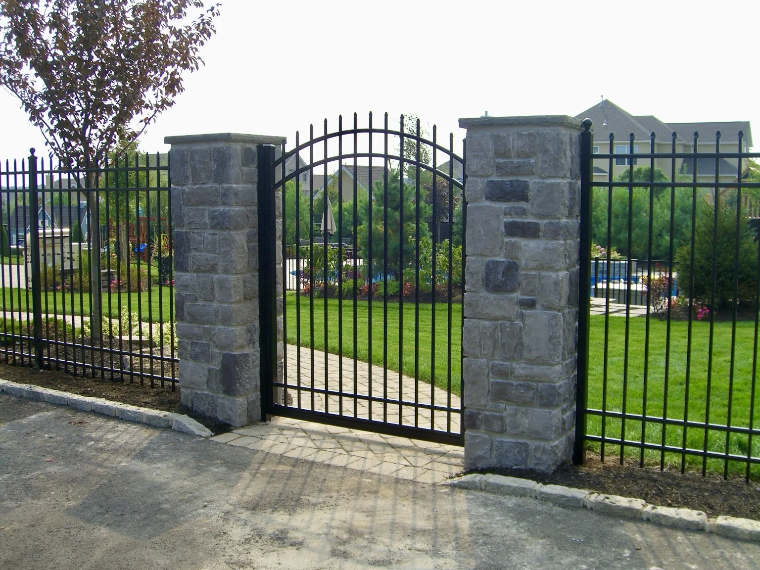 Arched black aluminum gate centered between masonry columns in Miller Place, New York