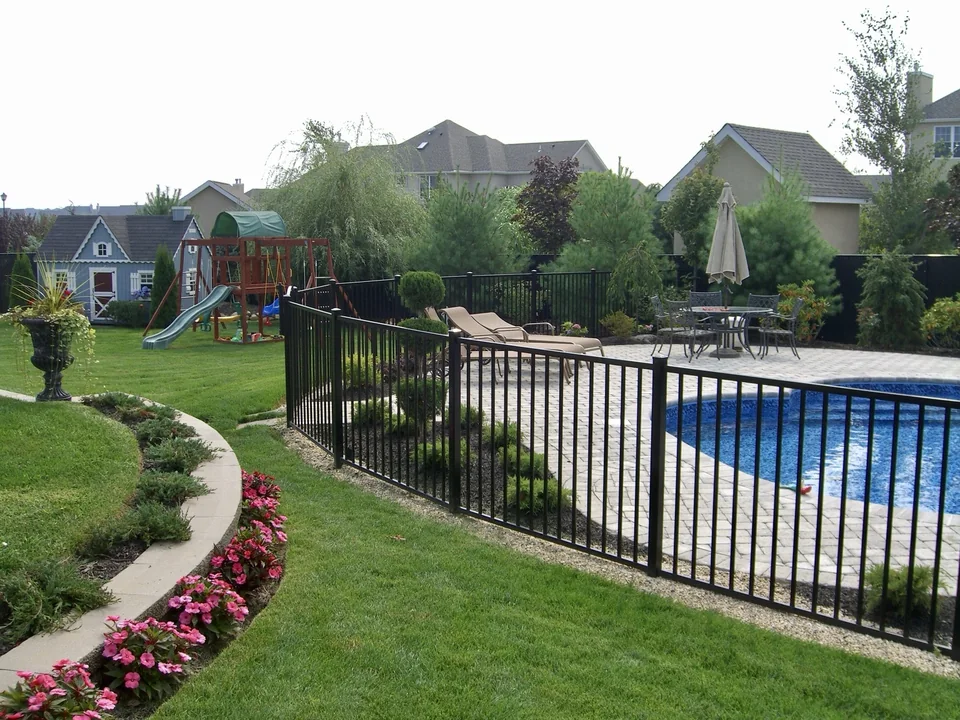 Black aluminum pool fence following a soft radius beside a landscaped pool in Miller Place, New York