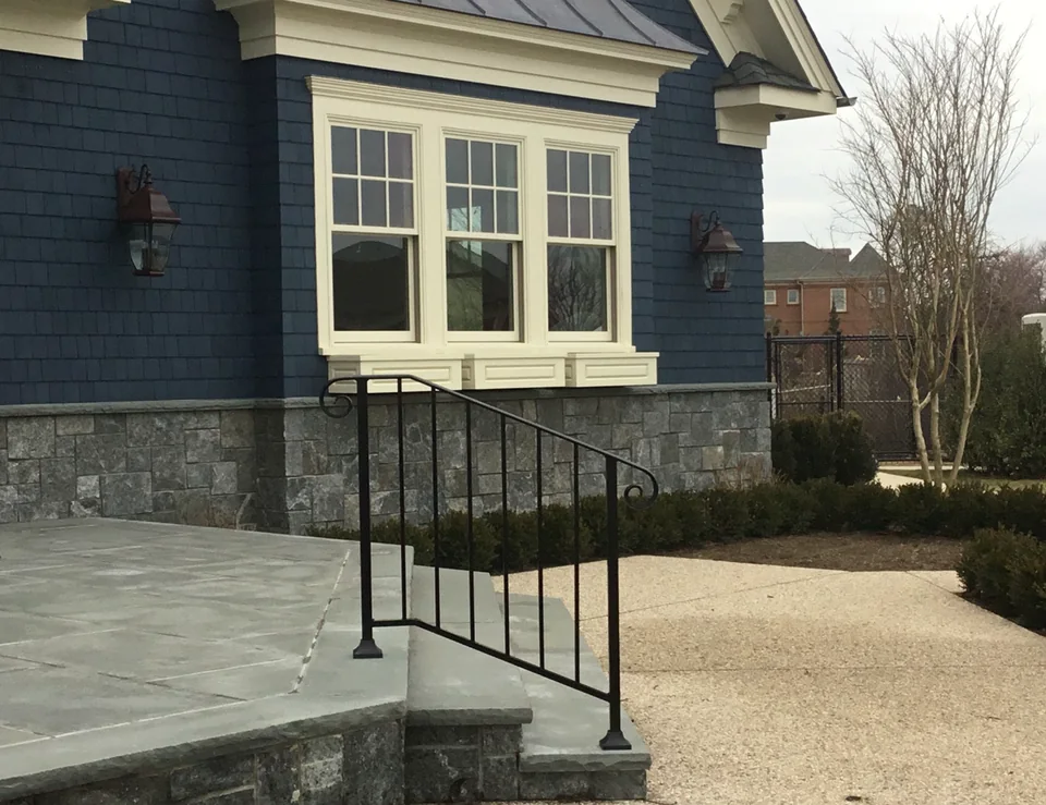 Custom black powder-coated aluminum handrail on stone exterior steps at a blue waterfront home in East Islip, New York