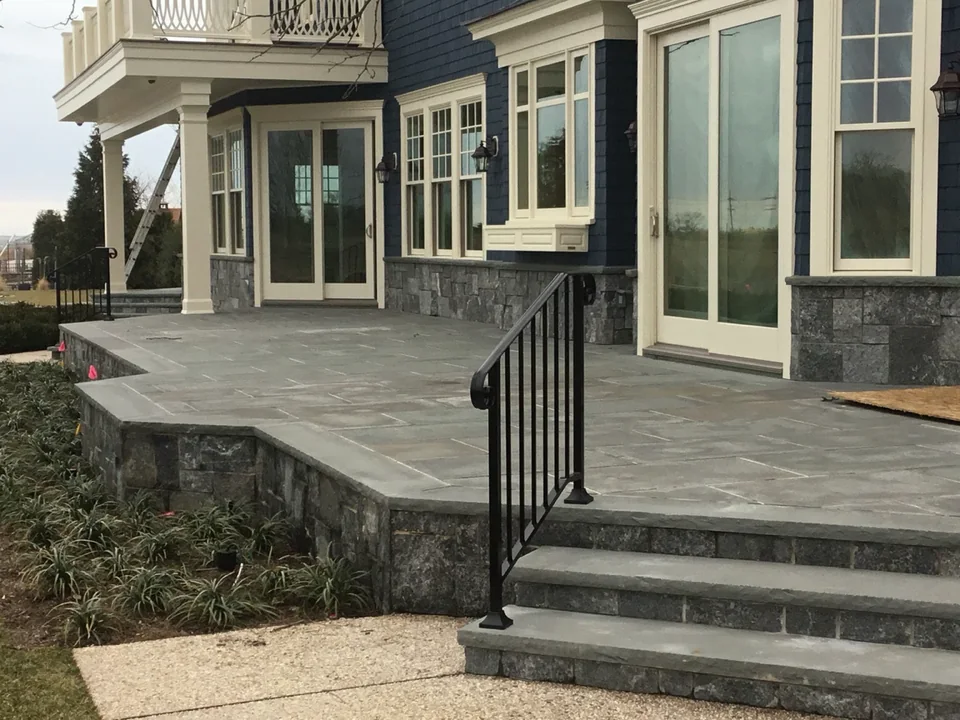 Custom black aluminum handrail at a second exterior stair run beside the stone terrace of a waterfront East Islip home