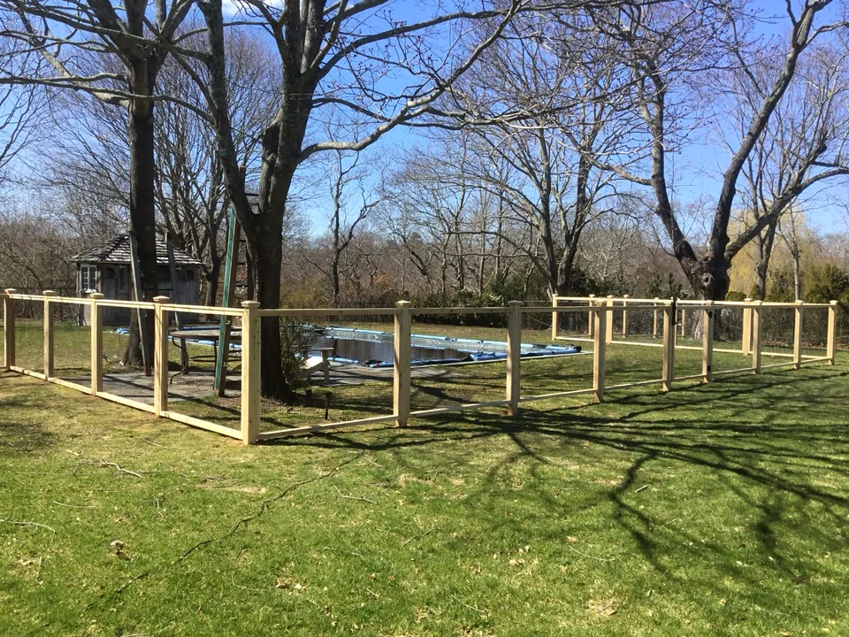 Corner return of the cedar framed-wire pool fence around mature trees in Center Moriches, New York.