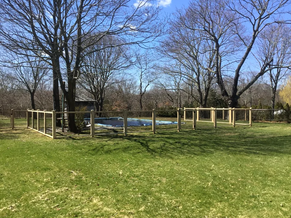 Wide landscape view of the custom cedar and black wire pool enclosure in Center Moriches, New York.