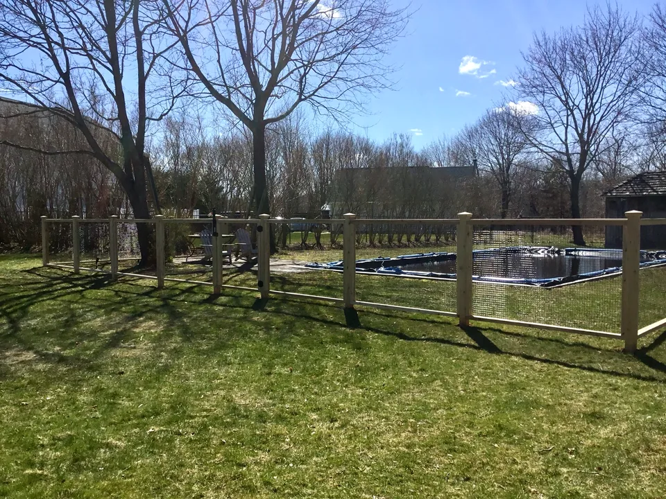 Long run of cedar framing with black vinyl-coated welded wire beside the pool in Center Moriches, New York.