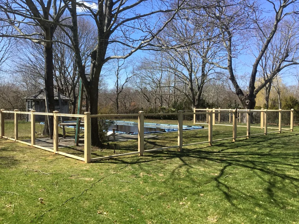 Wide view of the 48-inch cedar framed-wire pool fence turning around the pool lawn in Center Moriches, New York.