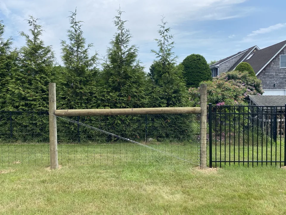 Round-post deer fence meeting a black aluminum fence and gate