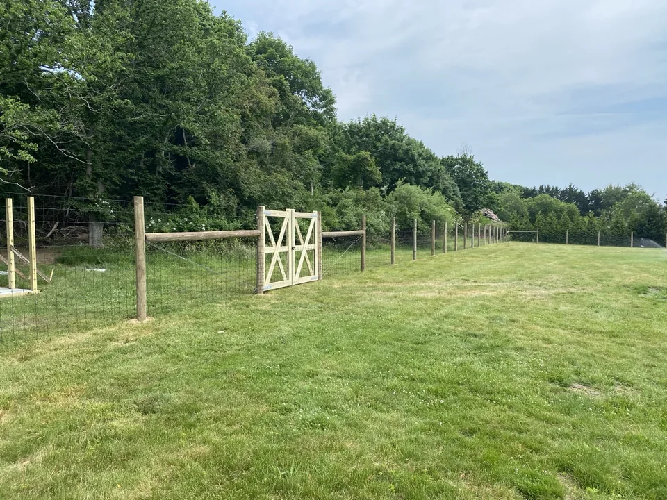 Braced wood gate set into a round-post deer fence across open lawn