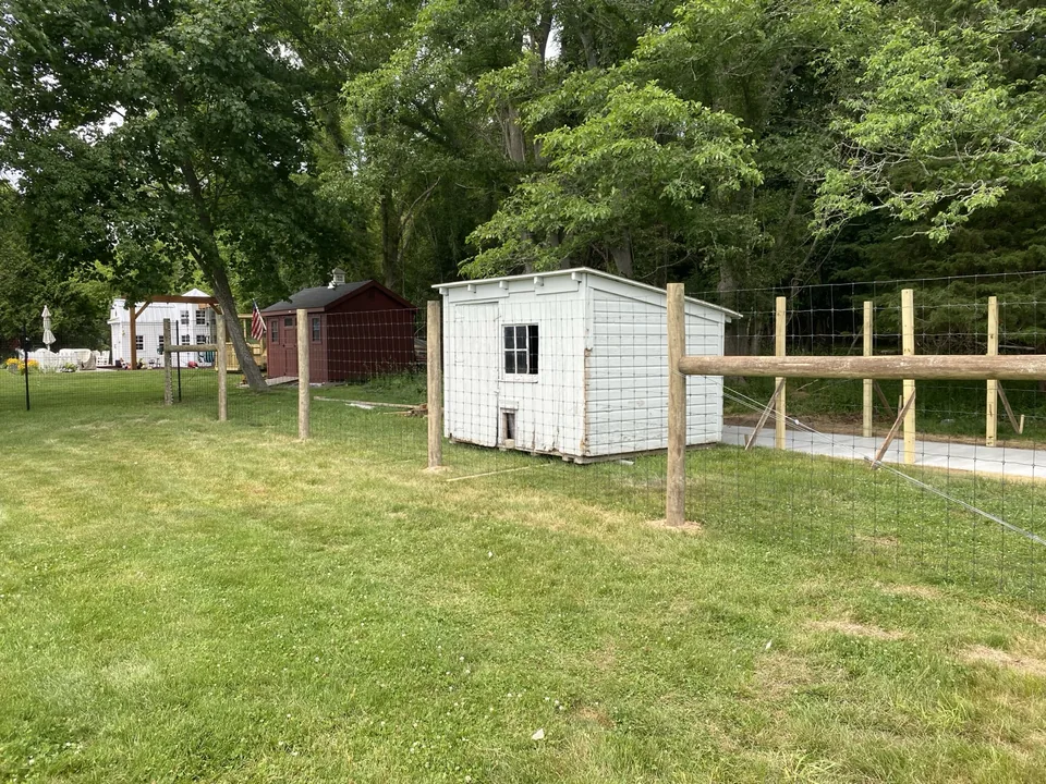 Round-post deer fence running past an outbuilding on a residential property