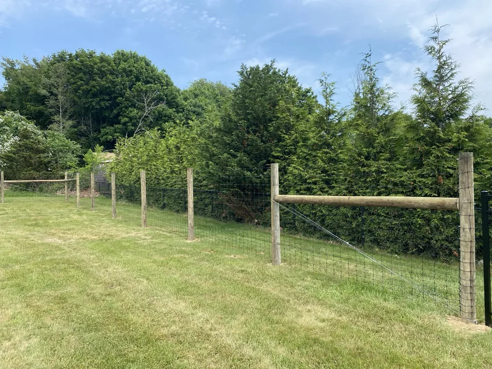Wide view of a round-post deer fence enclosing an open lawn