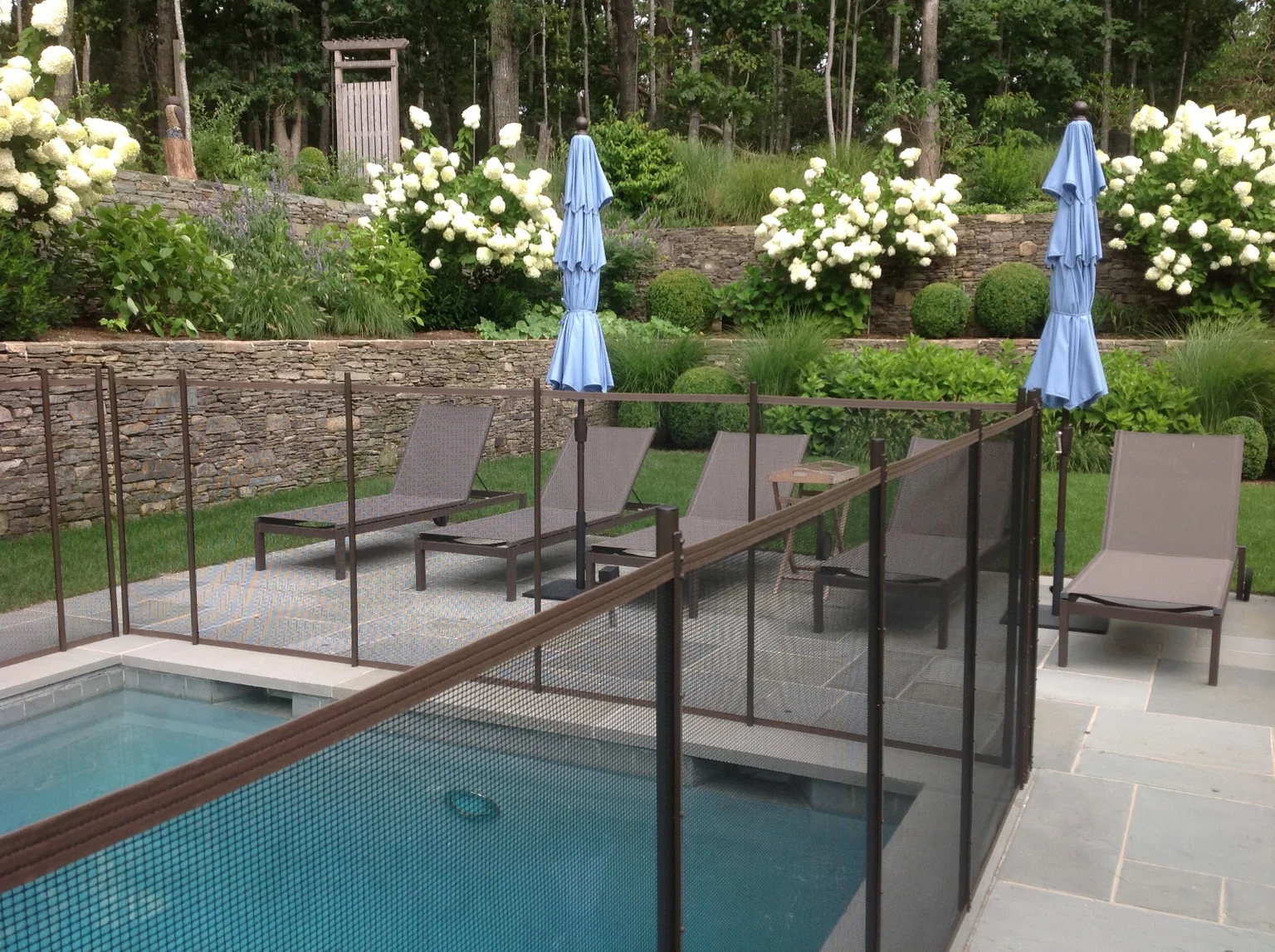 Brown Guardian pool fence surrounding a lounge area beside the landscaped East Hampton pool