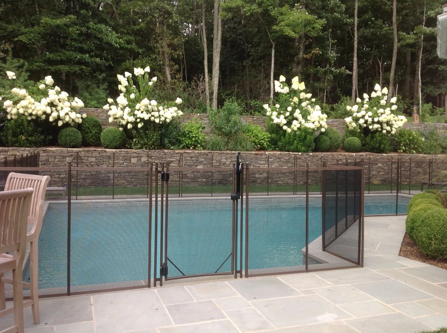 Brown Guardian pool fence and gate with stone retaining wall and hydrangeas in East Hampton
