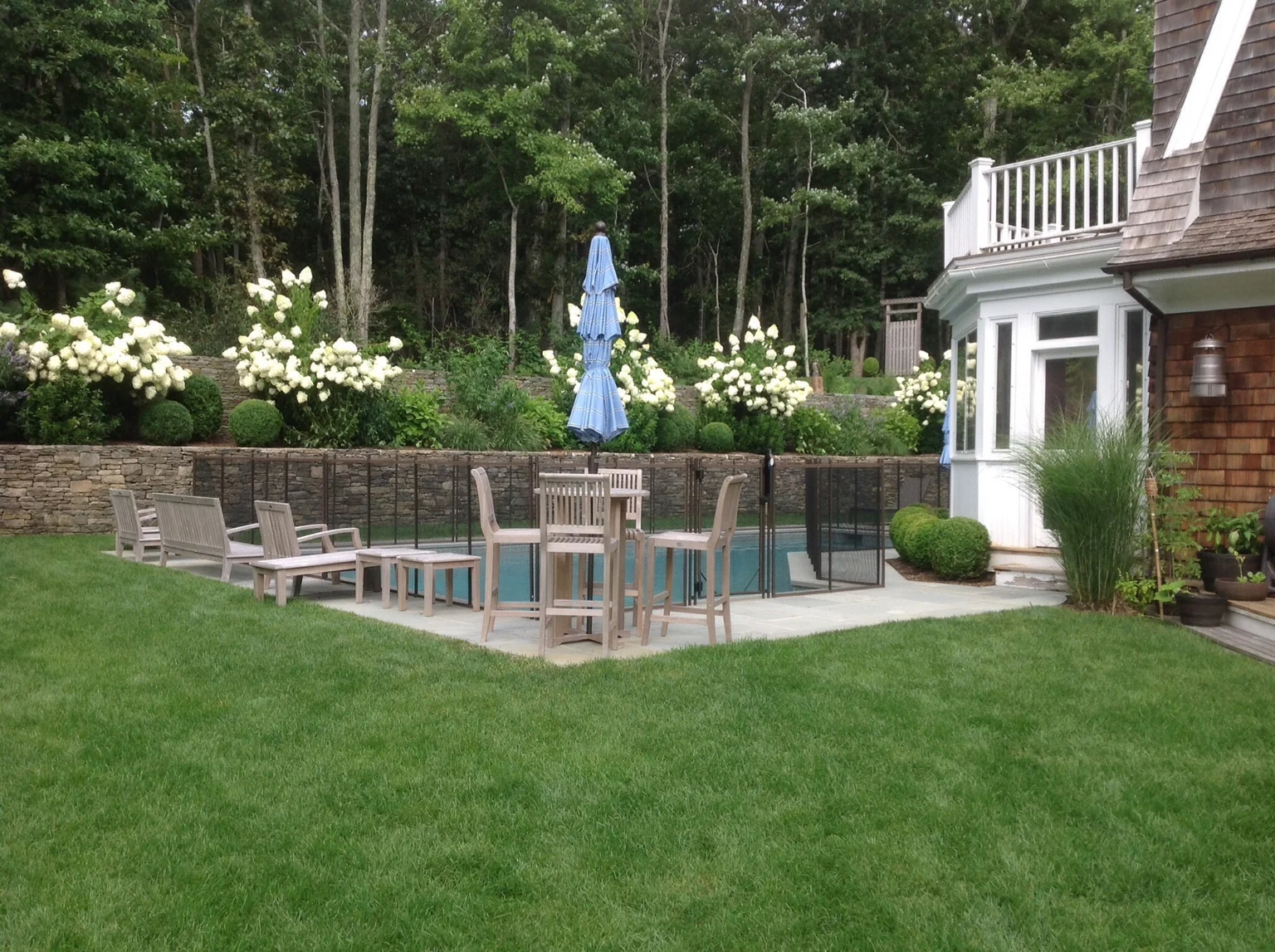 Wide view of the landscaped East Hampton pool area with brown Guardian removable mesh fencing