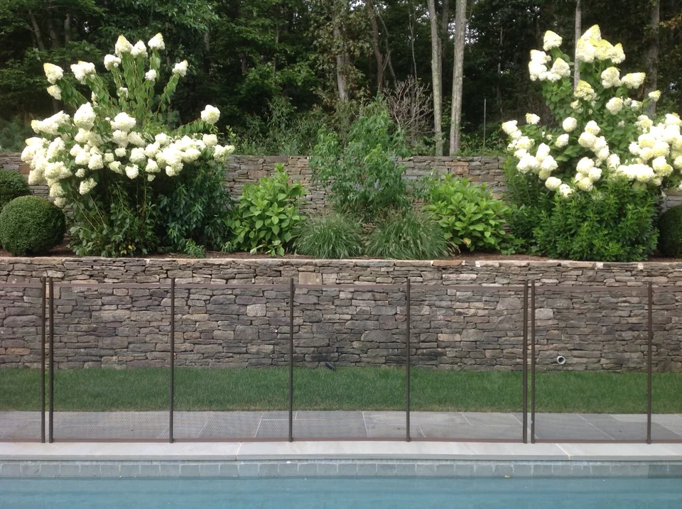 Brown Guardian mesh fence against a stone retaining wall and white hydrangeas in East Hampton
