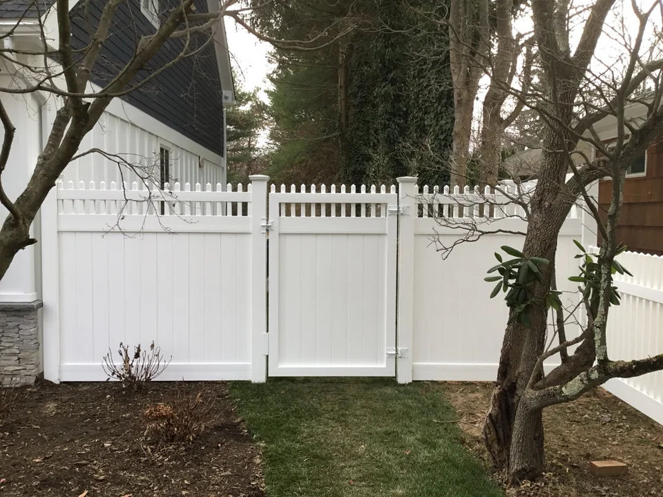 White PVC privacy gate and fence field-fitted through a steep grade transition in Locust Valley, New York