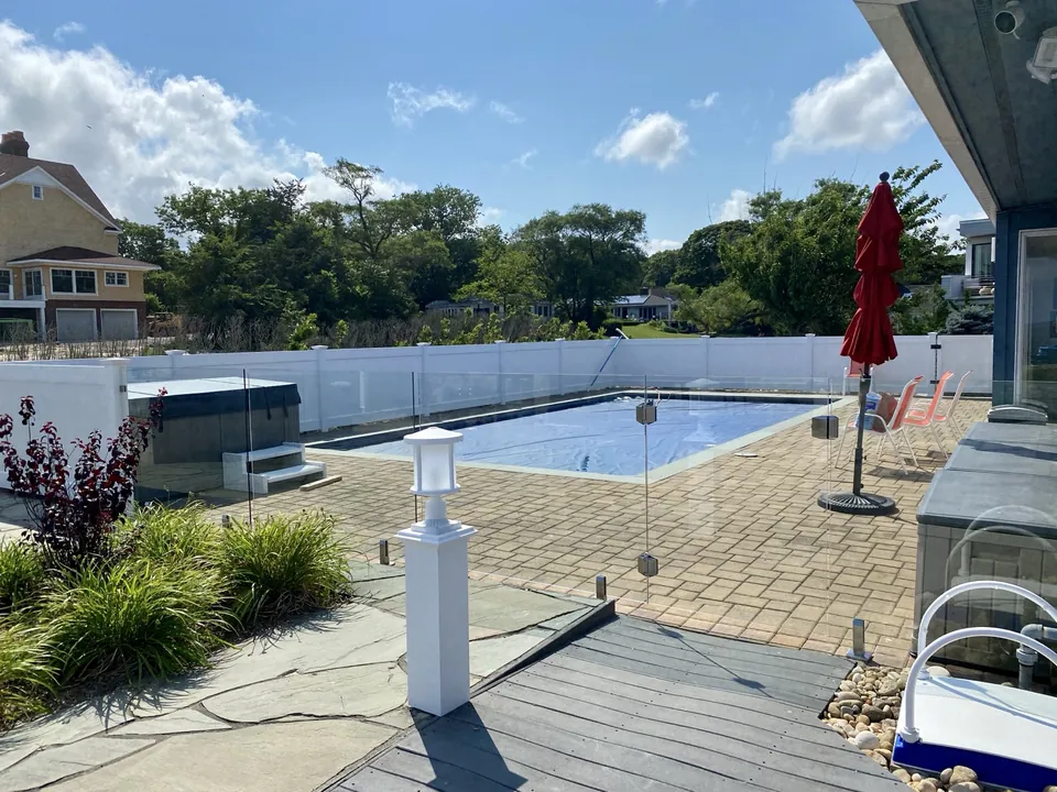 Glass pool safety fence surrounding a waterfront pool and spa area in Southold, NY.