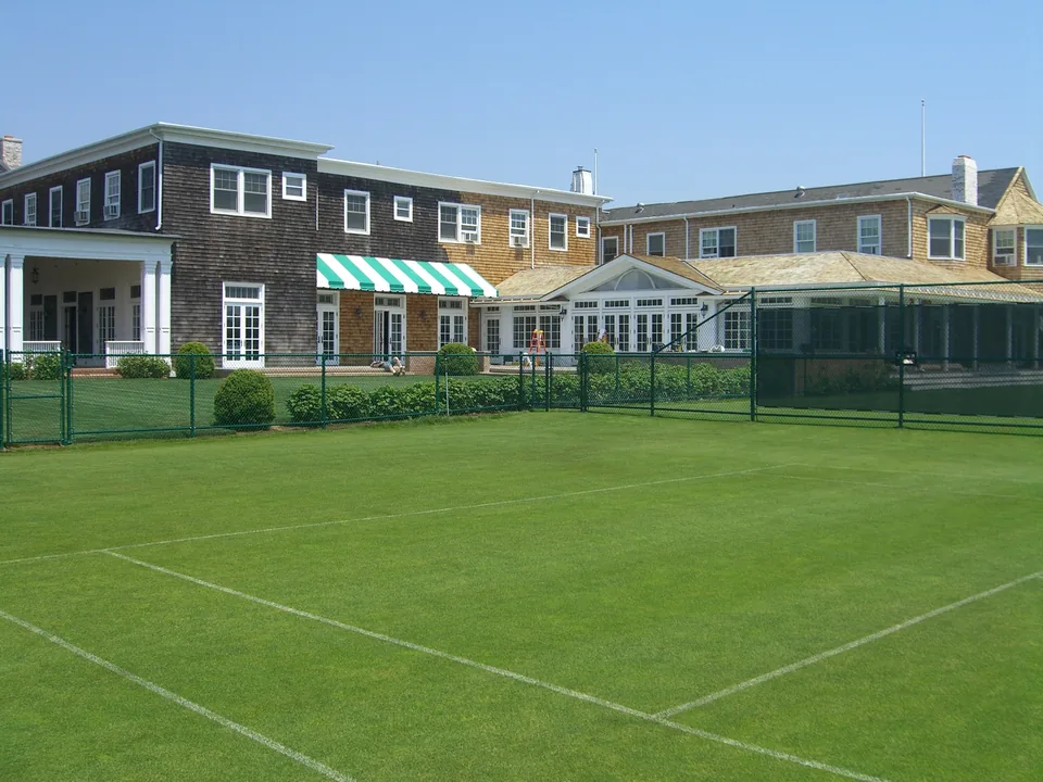 Wide view of a green chain link tennis court enclosure at a private tennis club in Southampton, New York