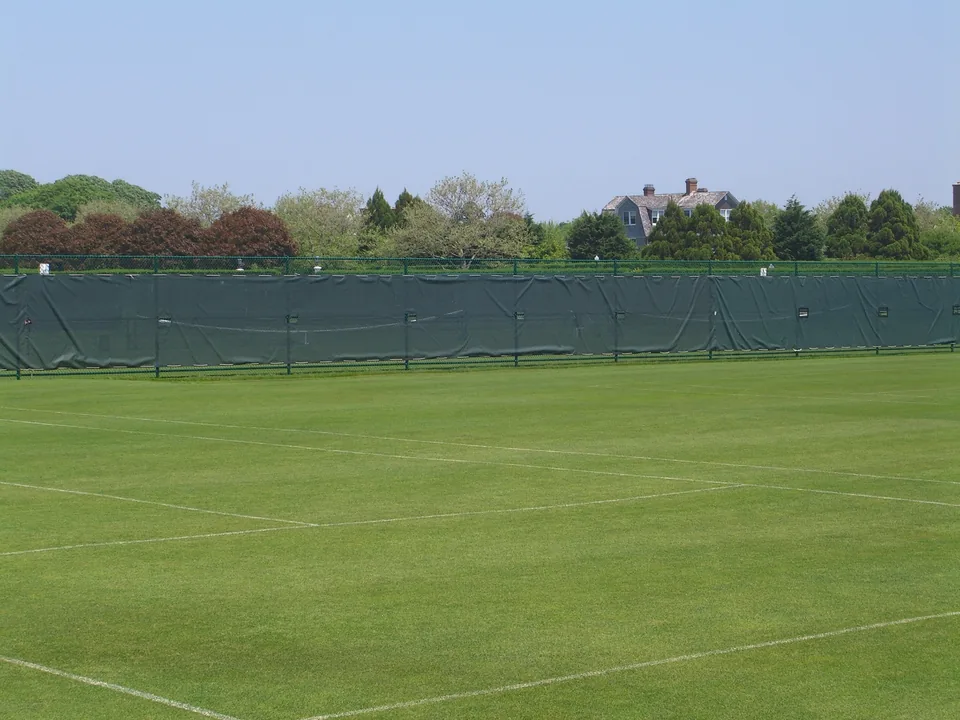 Green chain link tennis court enclosure with windscreen at a private tennis club in Southampton, New York