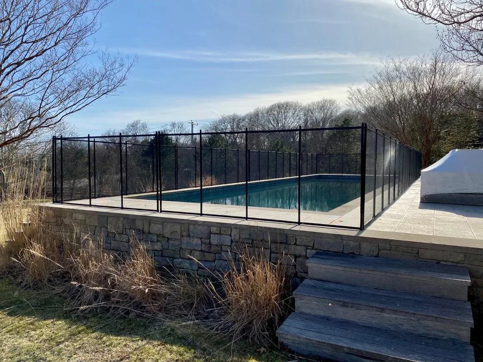 All-black removable mesh pool fence aligned along a raised Montauk pool terrace