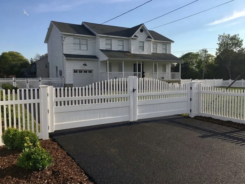 Angled view of a reinforced white PVC driveway gate and matching picket fence in Hampton Bays, New York.
