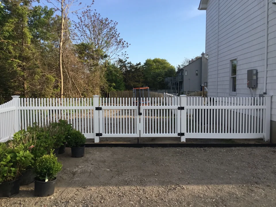 Rear-side job-site view of white PVC gates and picket fencing at a Hampton Bays property.