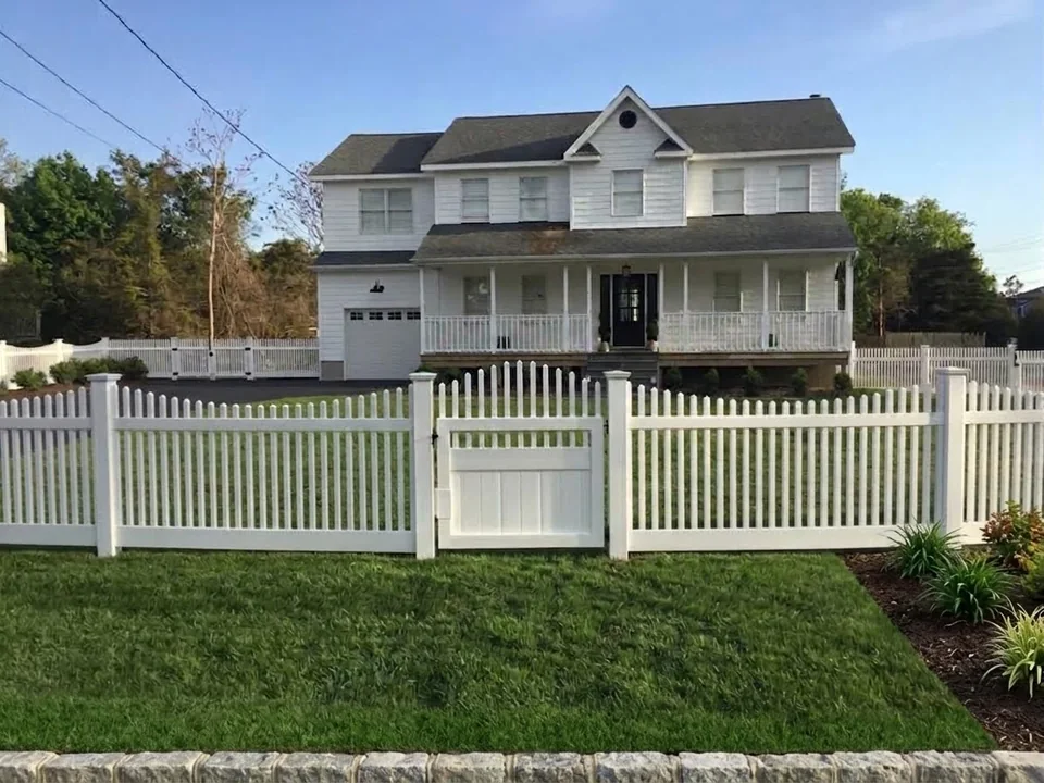 White PVC picket fence and matching walk gate across the front of a Hampton Bays home.